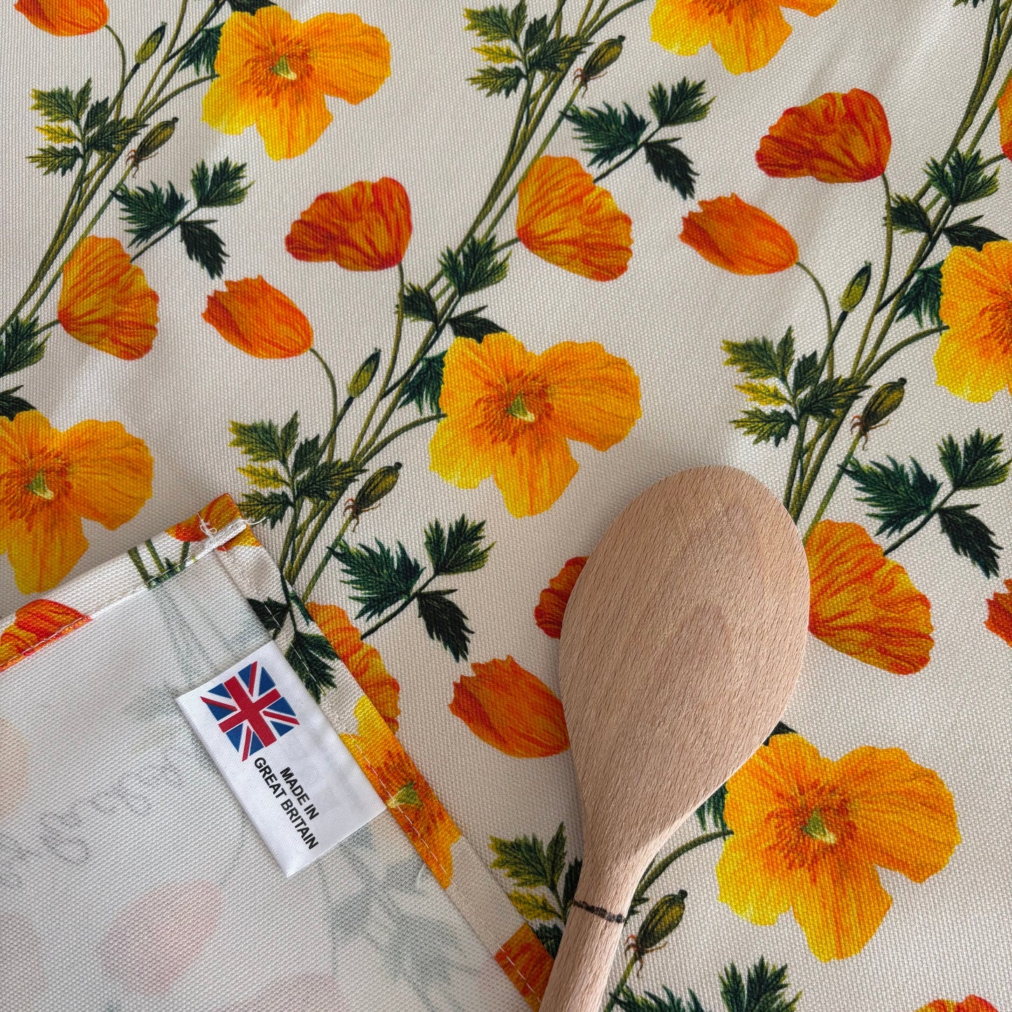 Floral Welsh poppy tea towel created from hand painted illustrations next to a wooden spoon 