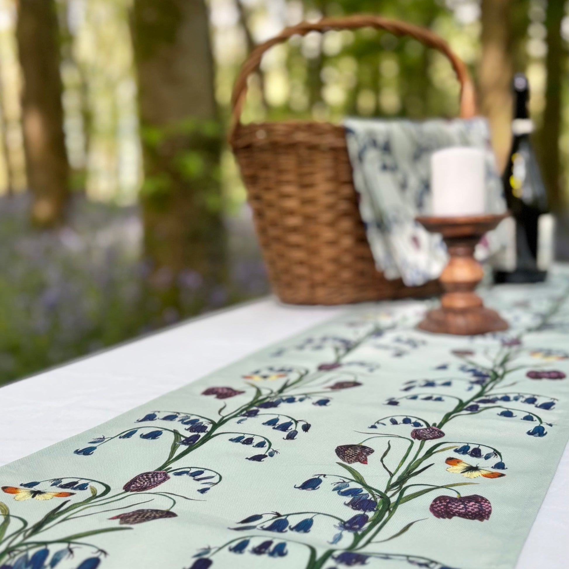 Table with floral bluebell and snake head fritillary table runner, basket, and candle outdoors