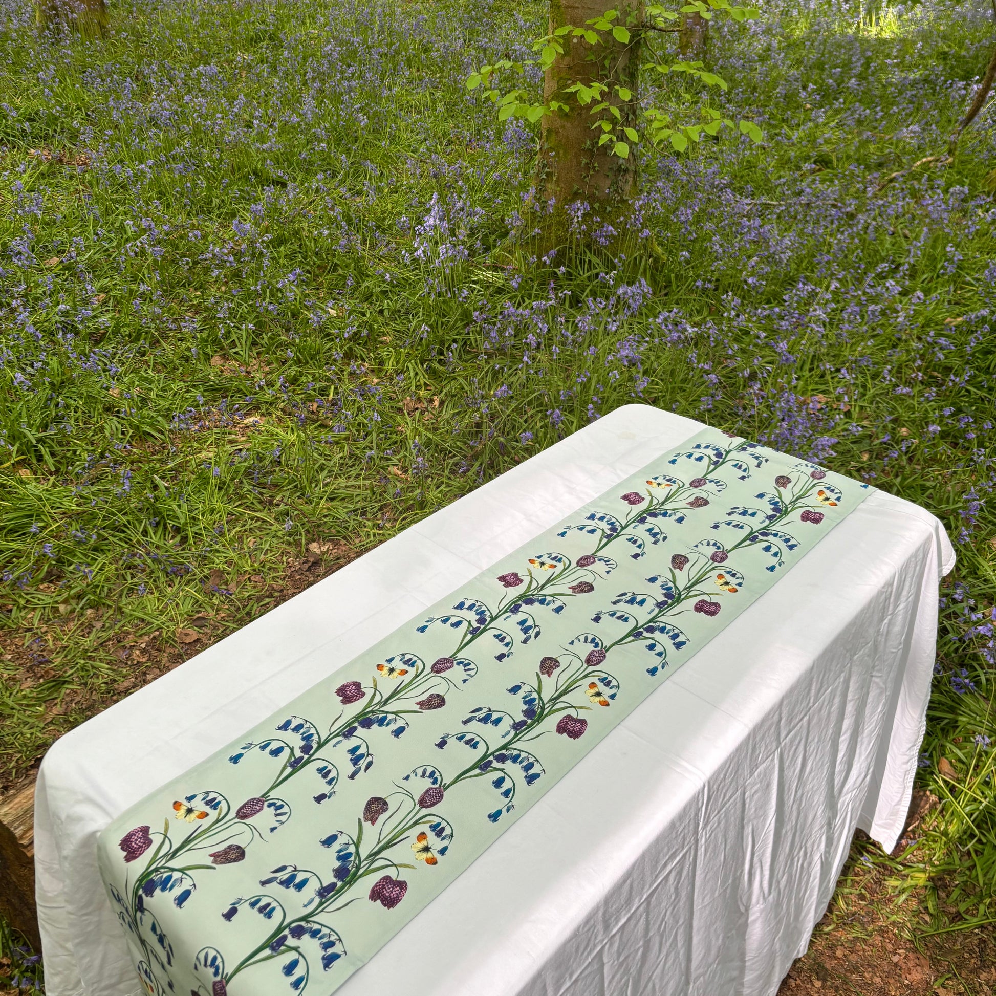 Floral table runner with bluebell and snake head fritillary pattern in a forest setting