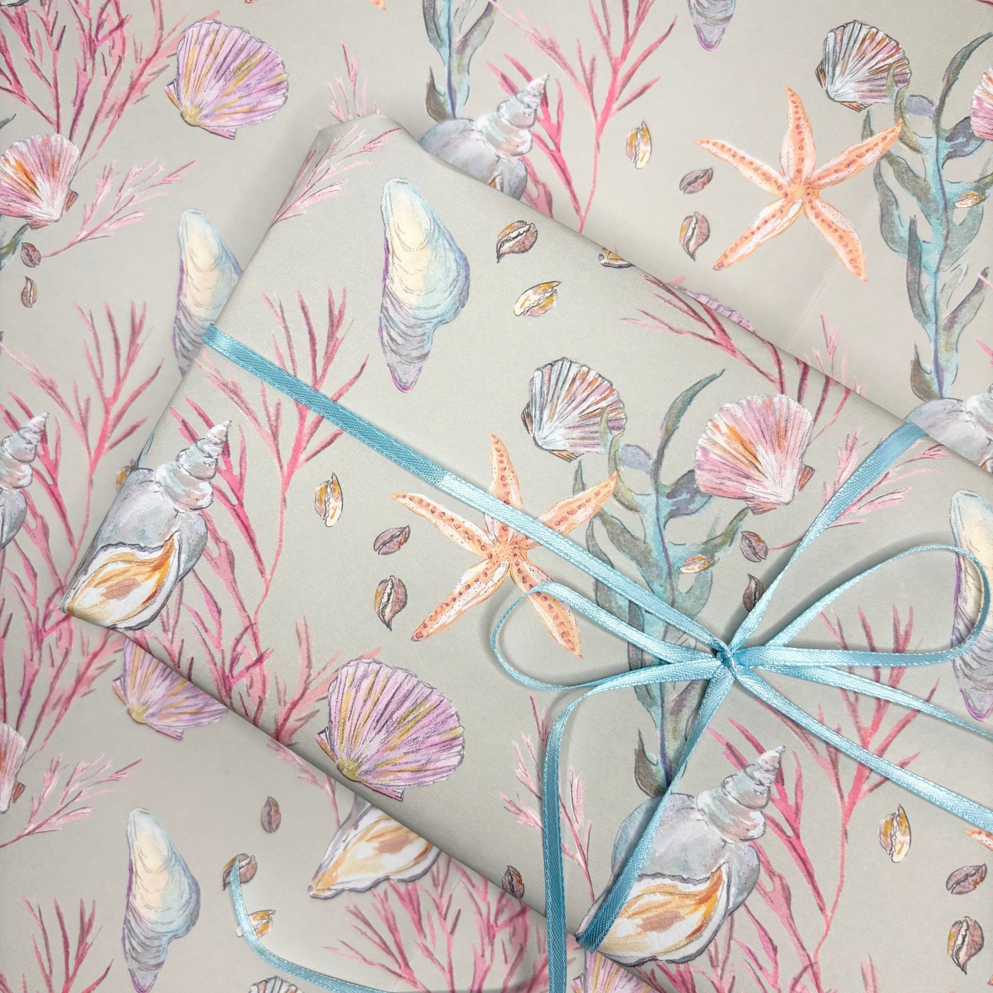 Gift wrap in seashell and starfish patterned paper with blue ribbon.