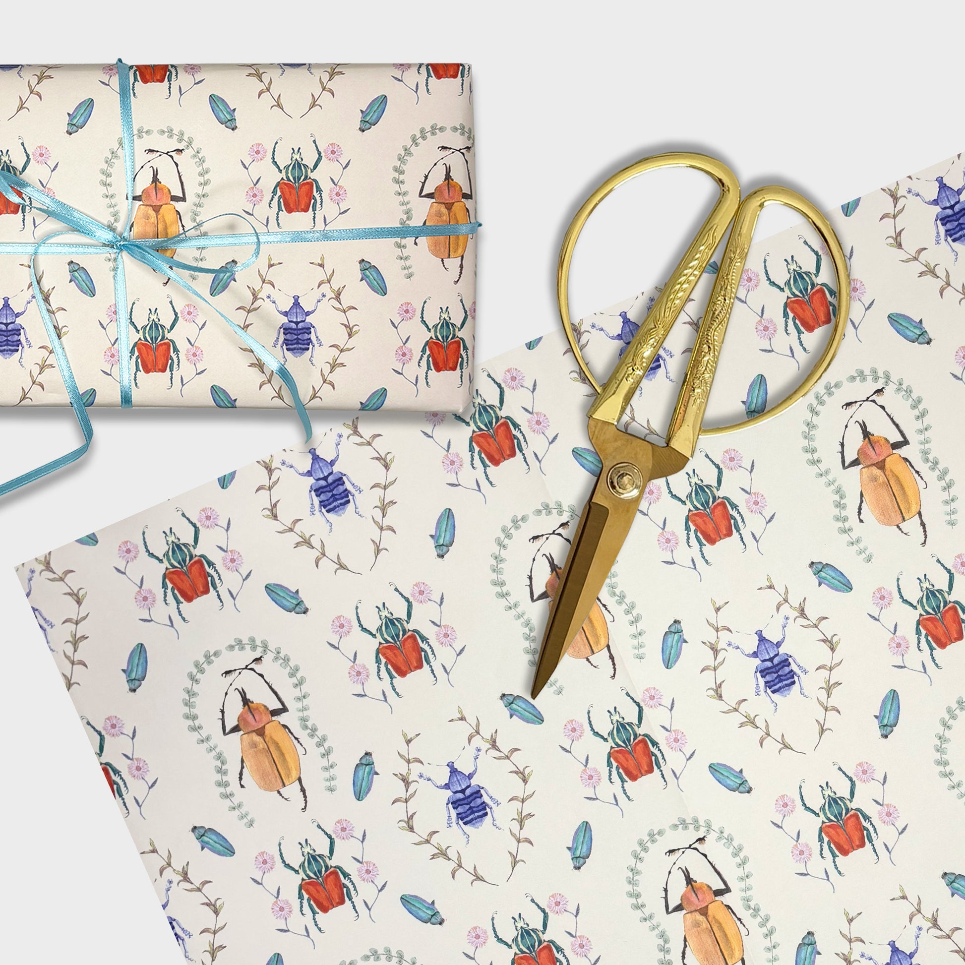 Gift wrap with hand painted beetle pattern, scissors, and blue ribbon on a matching background