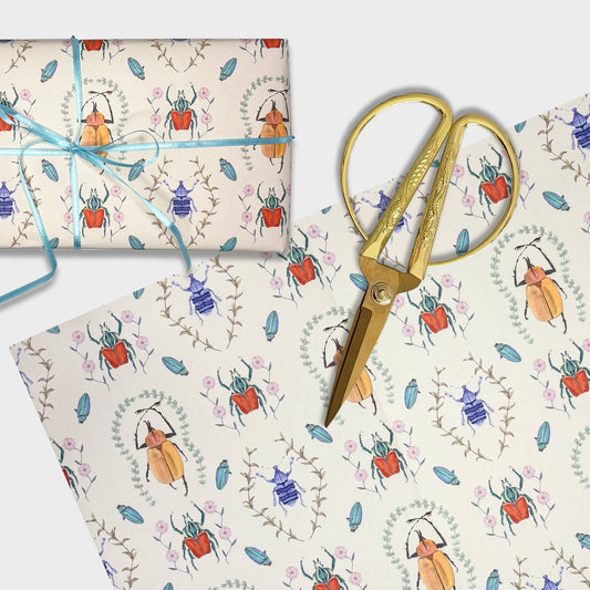 Gift wrap with hand painted beetle pattern, scissors, and blue ribbon on a matching background