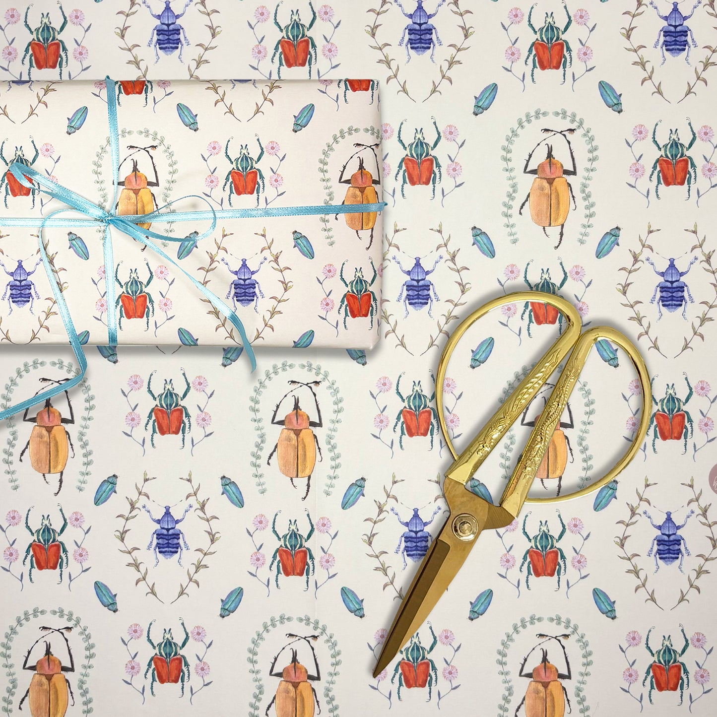 Gift wrap with hand illustrated beetle pattern, scissors, and blue ribbon on a matching background for entomologists
