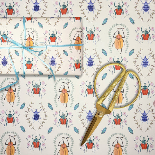 Gift wrap with hand illustrated beetle pattern, scissors, and blue ribbon on a matching background for entomologists
