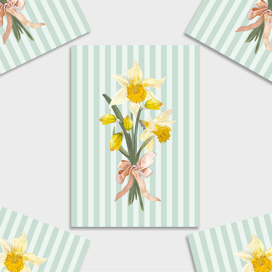 A mini art print featuring a watercolour bouquet of yellow daffodils tied with a pink ribbon, set against a mint green and white striped background. The print is displayed in a flat-lay arrangement with matching patterned paper corners visible around it.