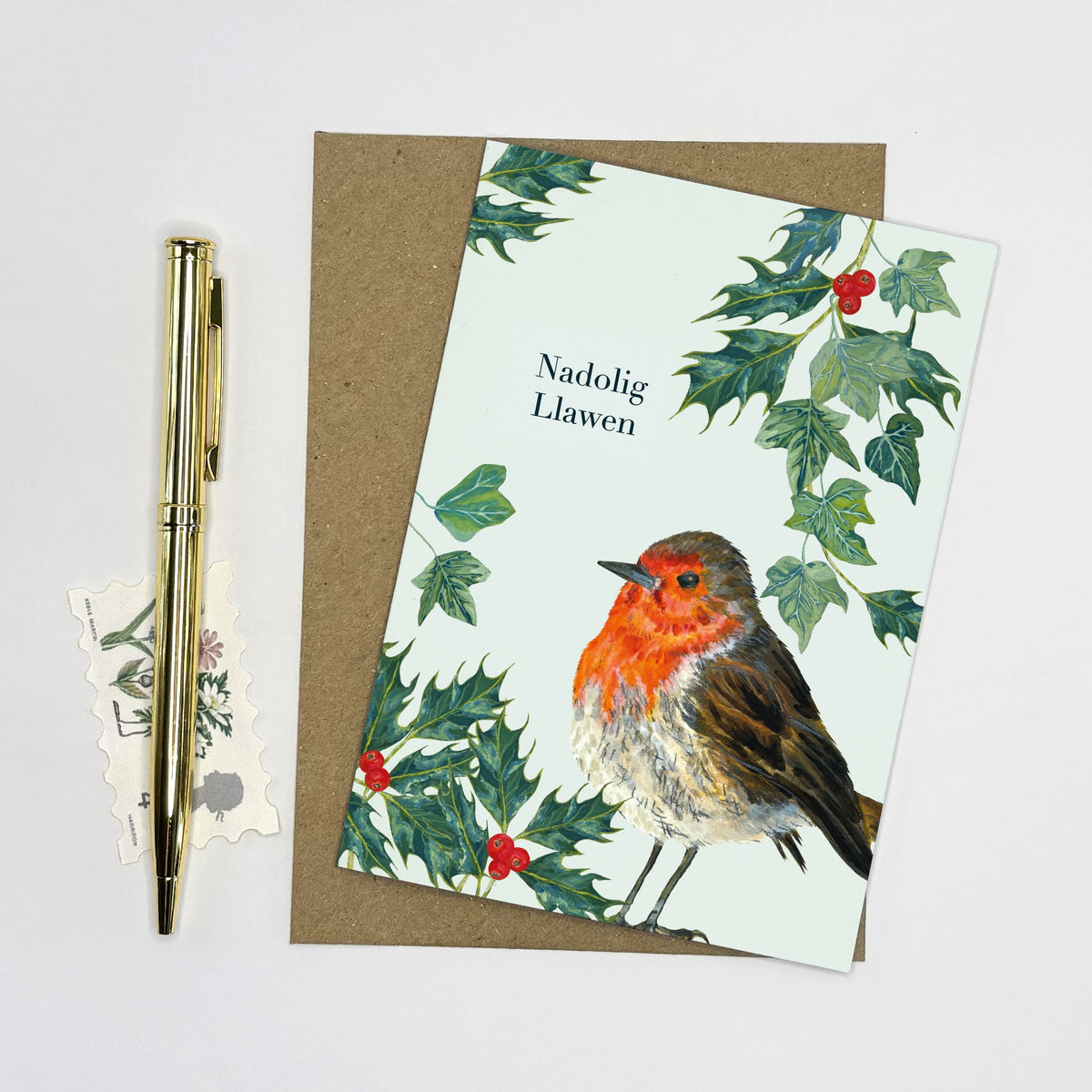 Robin hand illustrated Christmas card with festive green holly and ivy painting on a light blue background