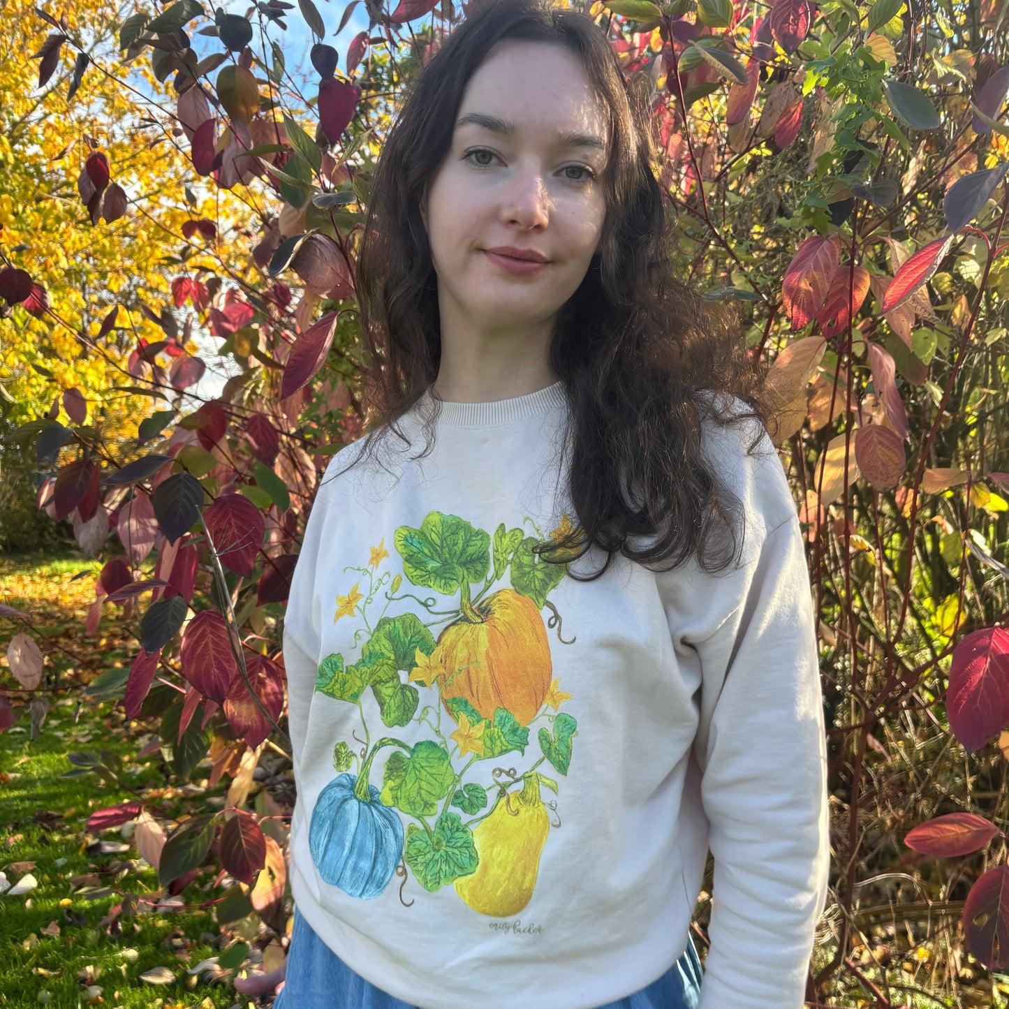 Girl with long brown curly hair wearing light oat coloured jumper with squash illustration 