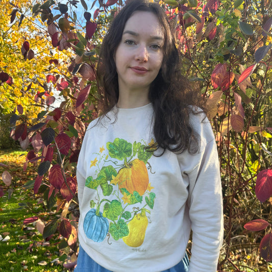 Girl with long brown curly hair wearing light oat coloured jumper with squash illustration 