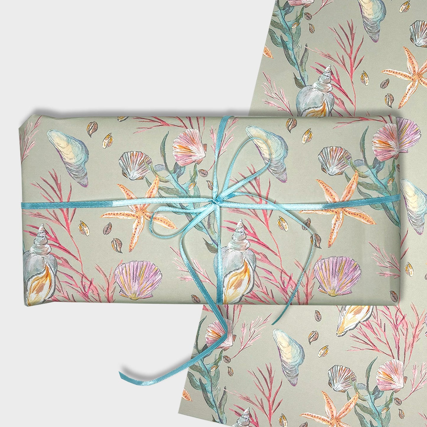 Gift wrapped in hand illustrated seashell and starfish patterned paper with blue ribbon on a light gray background