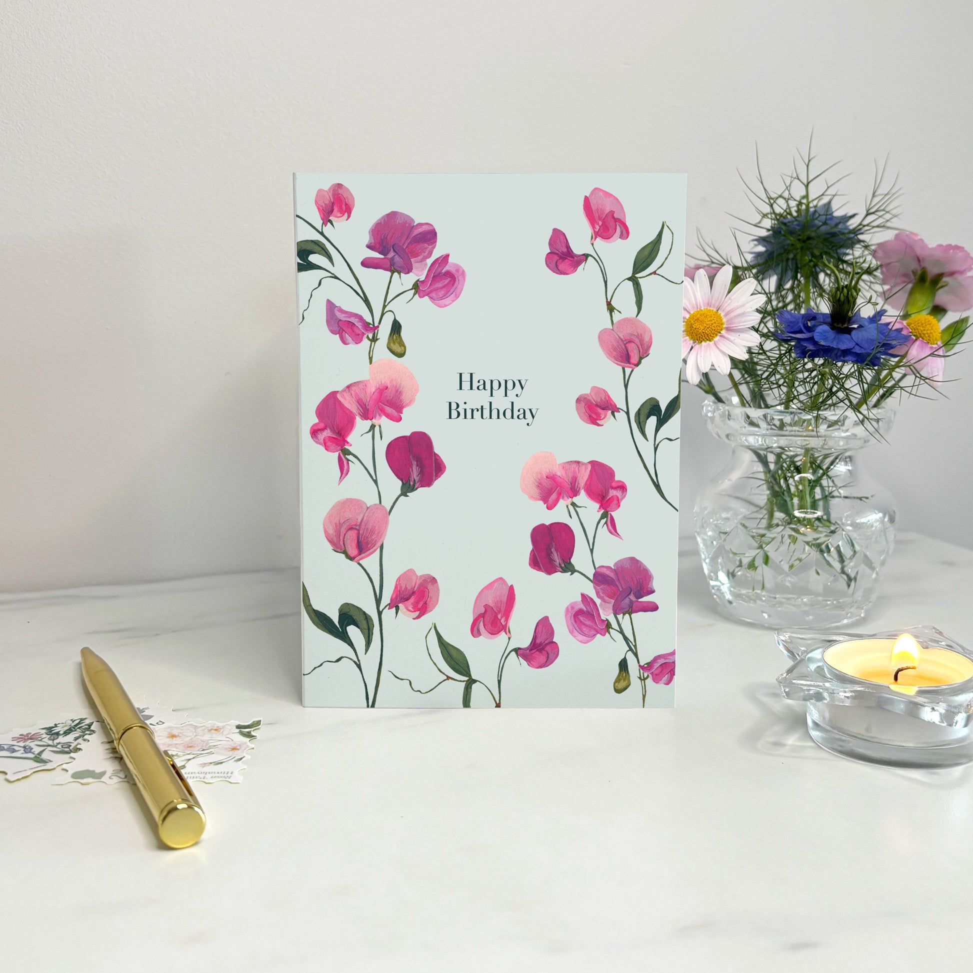 Sweet pea Floral summer birthday card with pink flowers on a white surface with a candle and vase.