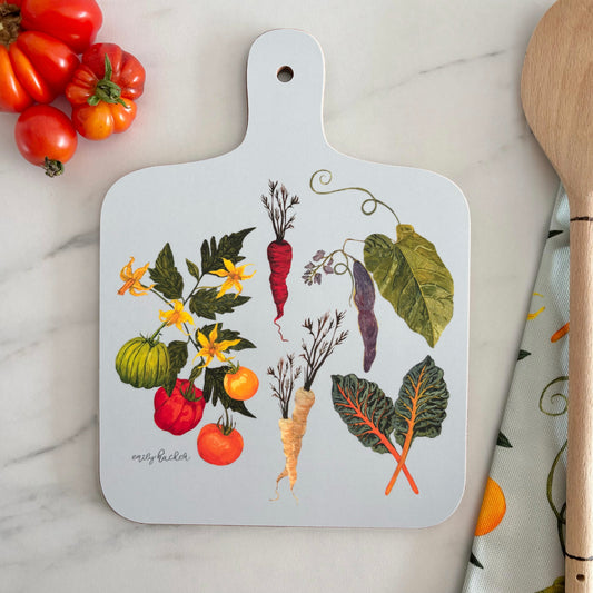 Heritage Vegetable hand painted chopping board with vegetable illustrations on a marble surface with tomatoes and a wooden spoon.