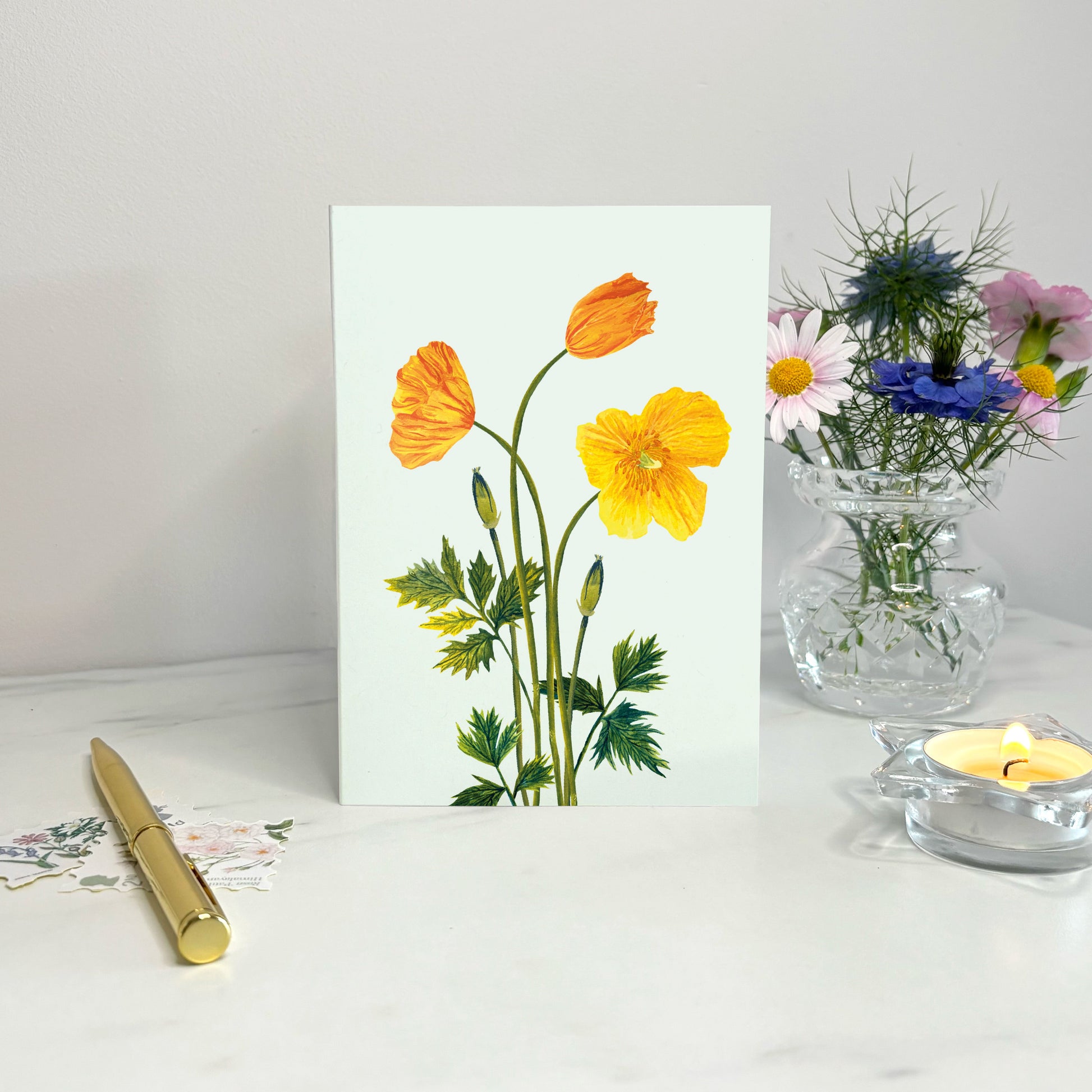 Floral wildflower card with yellow else poppy flowers on a white surface with a candle and vase in the background.